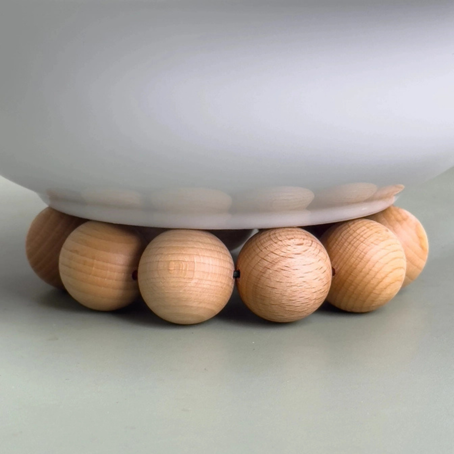 Gros plan sur les billes de hêtre massif et le cordon élastique du dessous de plat Nid sous une cafetière, montrant la qualité de finition.